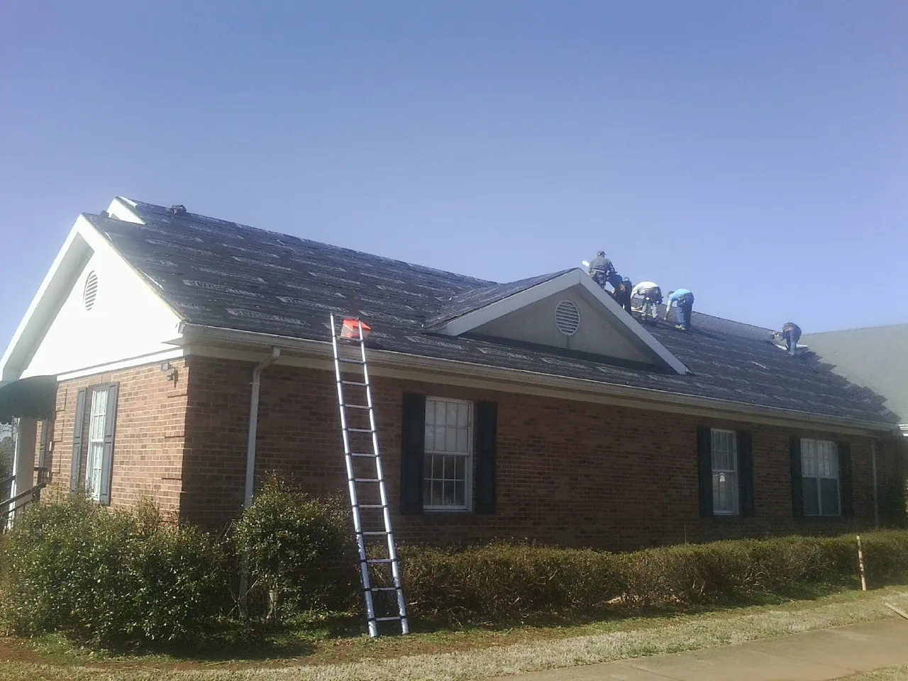 Crew tearing shingles off a brick ranch roof with a ladder set — Metal Roof Repair work by our crew in Kirkwood