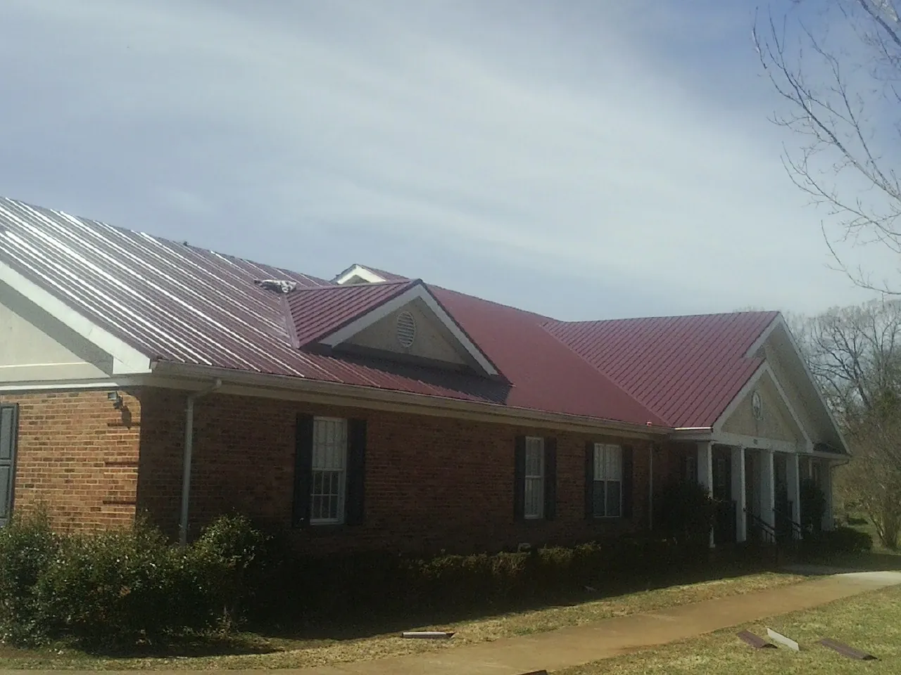 Red metal roof with gabled entries on a long brick building, from a Hail Damage Roof Repair job in Kirkwood